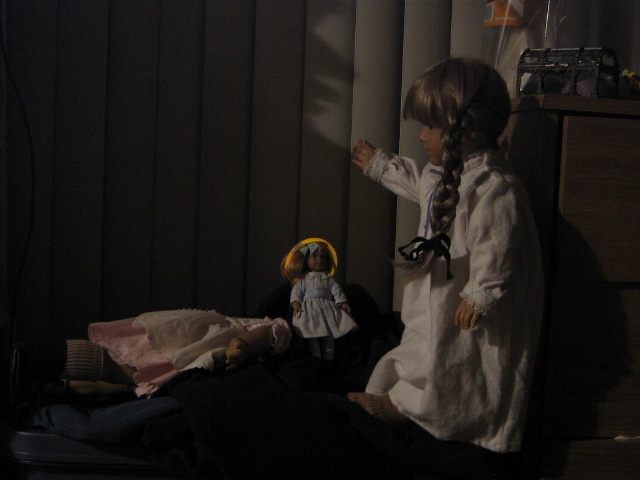 In the dark, Kirsten looks at a doll laying face-down, wearing her Birthday Dress.