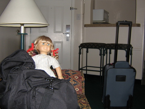 Kirsten in her summer outfit with red ribbons in a hotel room peeking out of a bag.